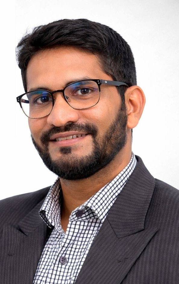 Moin, Registered Investment Advisor, smiling in a dark suit and glasses